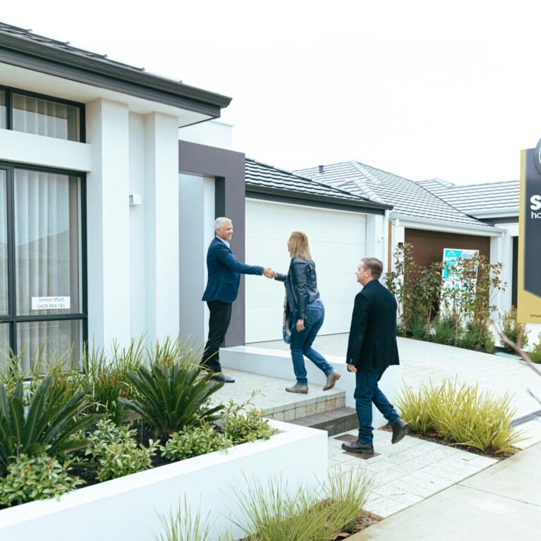 A realtor shakes hands with potential buyers outside a modern model home.