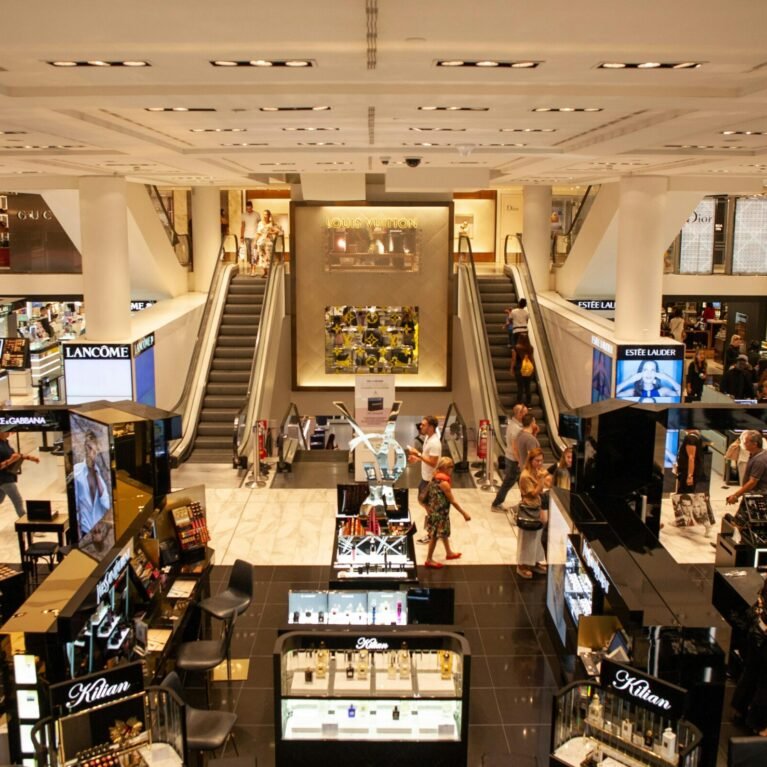 A bustling scene inside a modern shopping mall with escalators and various retail stalls.