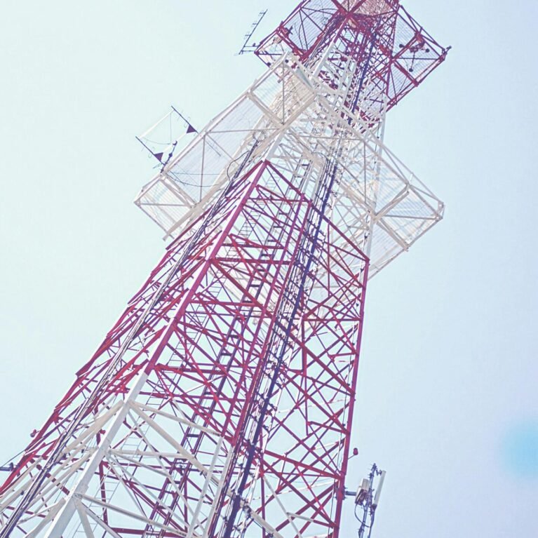 Low angle view of a red and white communication tower against a clear blue sky, capturing modern technology.