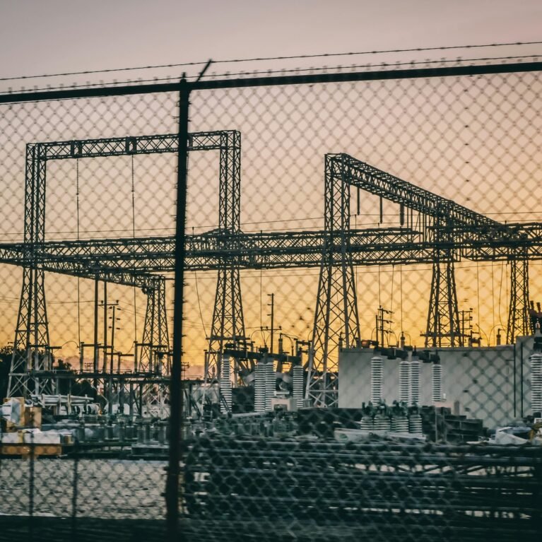 Industrial electric power substation photographed at sunset with fence in the foreground.