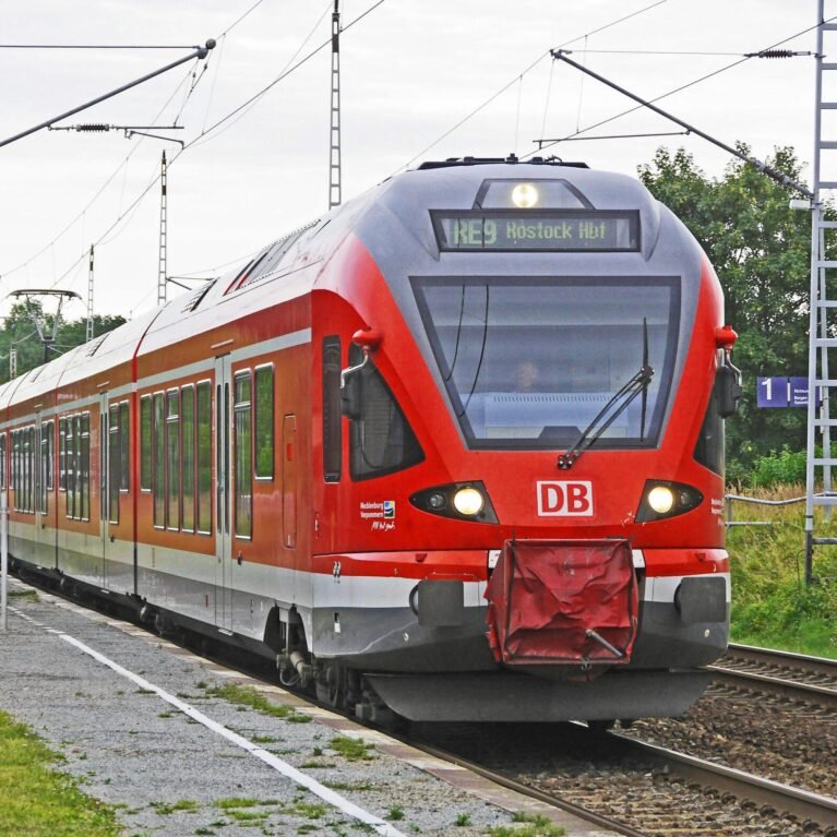 A vibrant red electric train arrives at a rural railway station, showcasing modern public transport.