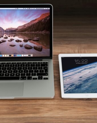 Modern workspace showcasing Apple laptop, tablet, and smartphone on a wooden desk.