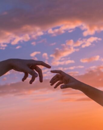 Crop anonymous people pulling hands to each other against bright sunset sky with clouds