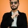 pexels-photo-997512-997512 Confident man in sunglasses posing against a vibrant orange backdrop.