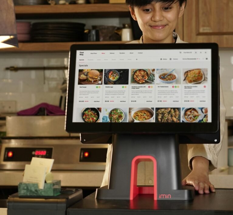A cashier uses a touchscreen system for taking orders in a restaurant setting.